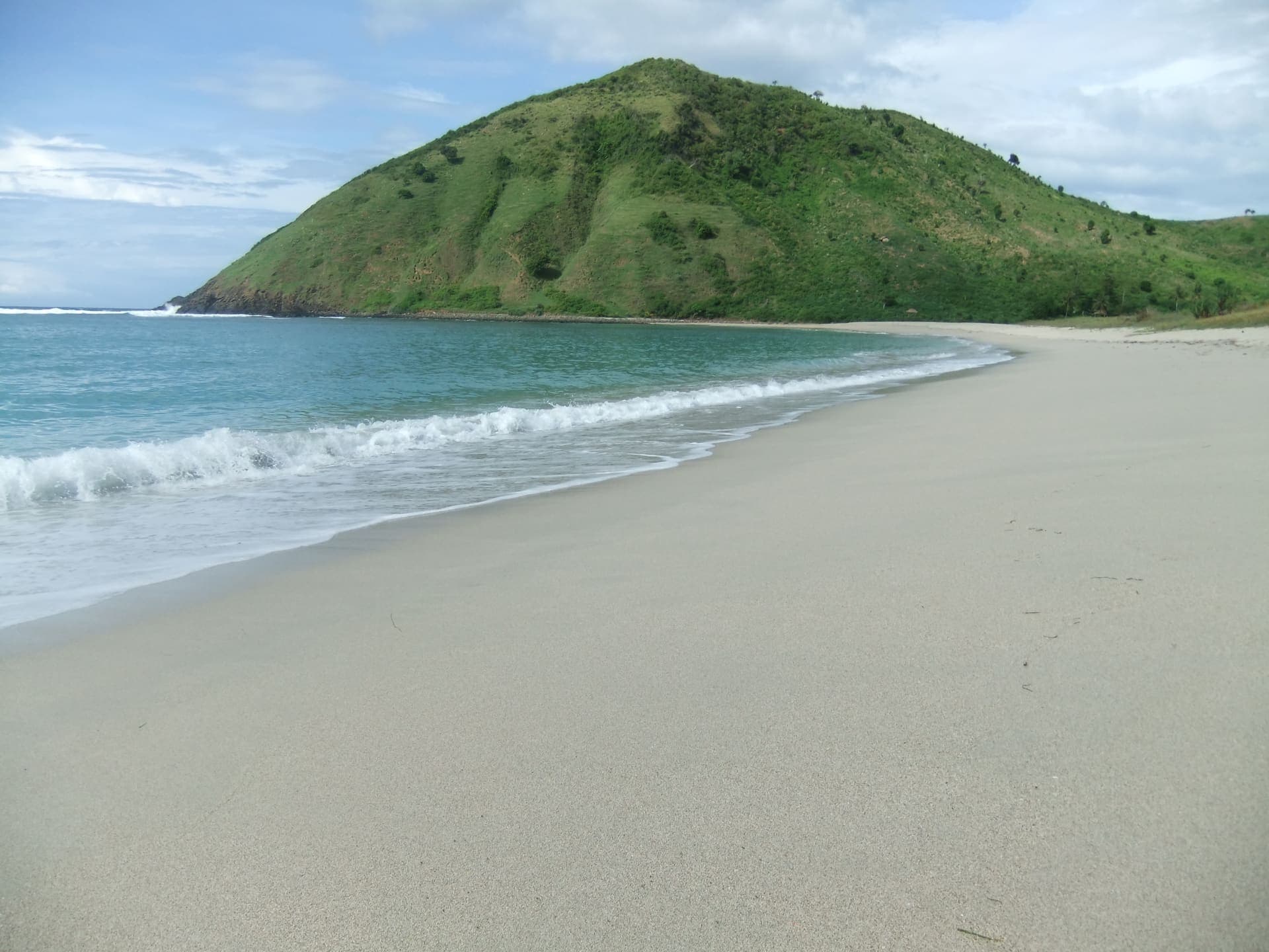 The curved white-sand bay of Mawun Beach below a green headland, South Lombok